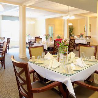 A well-lit dining room with neatly arranged tables and chairs, featuring elegant table settings.