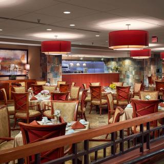 A well-decorated restaurant interior with neatly arranged tables and chairs, featuring warm lighting.