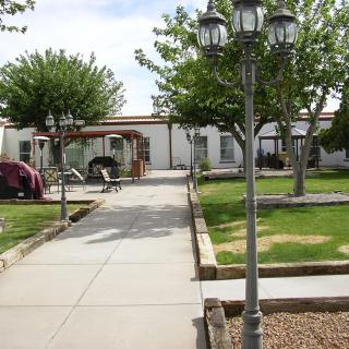 A peaceful garden area with a pathway leading to a building, flanked by lampposts and trees.