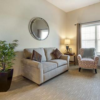 A cozy living room with a sofa, armchair, mirror, and decor elements such as a plant and lamp.