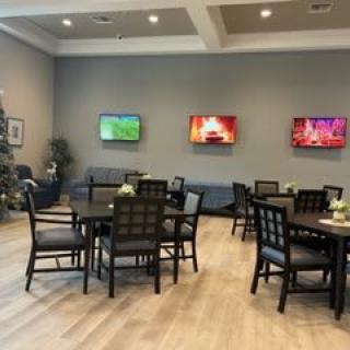 A cozy dining area with multiple tables, chairs, and wall-mounted televisions.