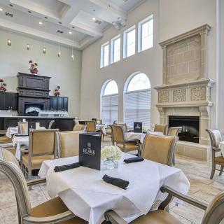 A spacious and elegant dining area with beautifully arranged tables, featuring large windows and a grand fireplace.