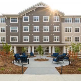 A modern residential apartment building with a landscaped courtyard featuring seating areas and pathways.