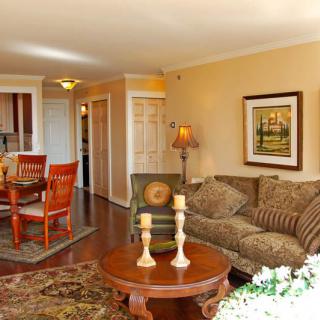 A cozy living room with a sofa, wooden coffee table, dining area, and decorative artwork on the wall.