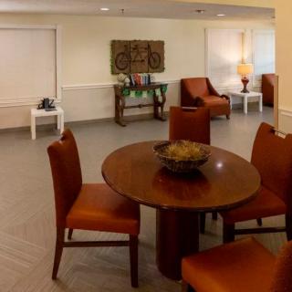 A cozy interior space featuring a round wooden table and chairs with warm tones, complemented by decorative elements and additional seating.