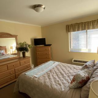 A cozy bedroom with a neatly made bed, wooden furniture, and natural light streaming through the window.