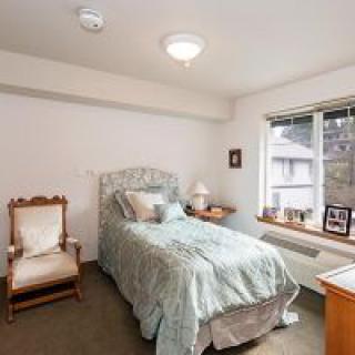 A cozy bedroom with a single bed, armchair, and a window allowing natural light.
