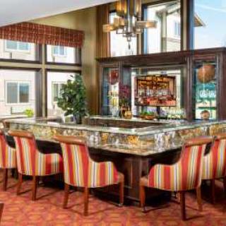 A stylish bar area featuring a marble countertop, striped upholstered chairs, and elegant wooden accents.
