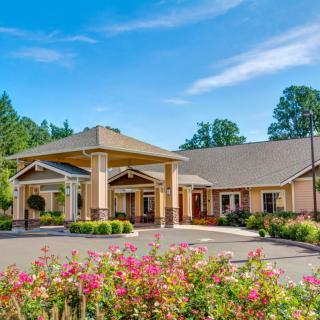 A well-maintained building with a welcoming entrance, surrounded by vibrant flowers and lush greenery under a clear blue sky.