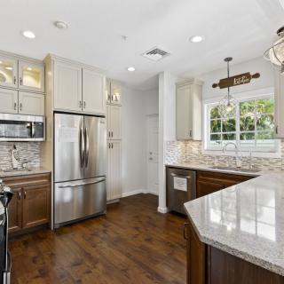 A modern kitchen with stainless steel appliances, white cabinets, and hardwood floors.