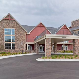 A large residential building with a stone facade and covered entrance, featuring a driveway leading up to the main doors.