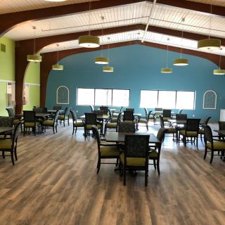A spacious dining area with multiple tables and chairs, featuring a wooden floor and modern lighting fixtures.