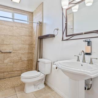 A modern bathroom with a spacious walk-in shower, pedestal sink, and tiled flooring.