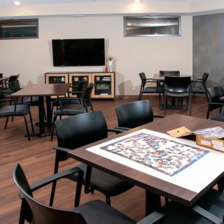 A cozy game room featuring tables, chairs, a television, and a puzzle in progress.
