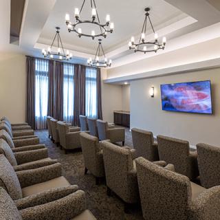 A luxurious theater room with comfortable seating and elegant chandeliers, featuring a large display screen.