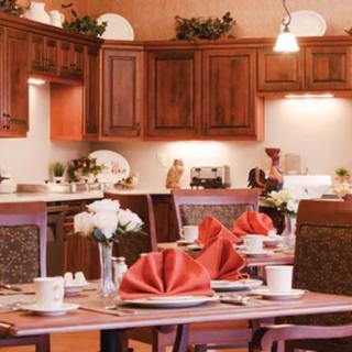 A warmly lit kitchen and dining area with elegantly set tables featuring red napkins and white flowers.