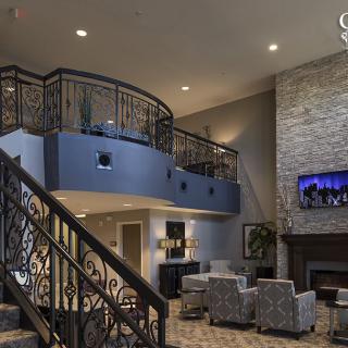 A modern living room interior featuring a loft with stylish railings, a cozy seating area by the fireplace, and a television mounted on the stone wall.