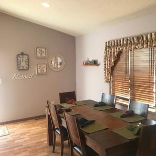 A cozy dining room with a wooden table and chairs, adorned with wall decorations and window blinds.
