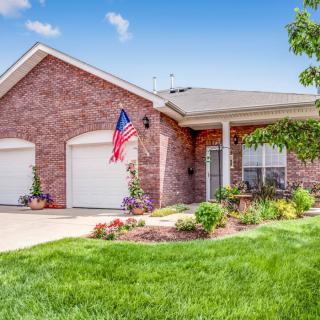 A suburban brick house with a well-maintained lawn, American flag, and two-car garage.