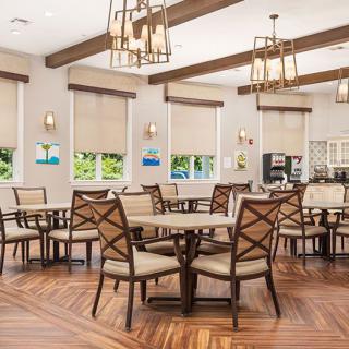 A well-lit dining area with wooden floors, round tables, and cushioned chairs under stylish ceiling lights.