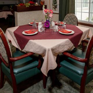 A beautifully arranged dining table featuring an octagonal tablecloth, elegant chairs, and a centerpiece of flowers.