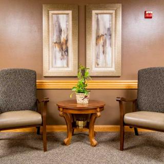 A waiting room with two chairs, a small wooden table with a plant, and abstract artwork on the wall.