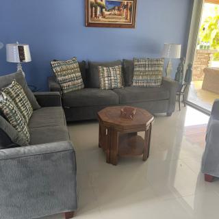 A cozy living room with blue walls, featuring comfortable sofas, patterned cushions, a round wooden coffee table, and decorative lamps.