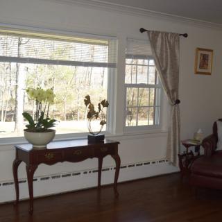 A cozy living room with a large window, adorned with curtains and a console table holding potted plants.