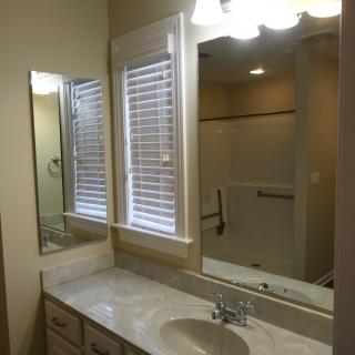 A clean and modern bathroom features a large mirror, marble countertop, and shower area.