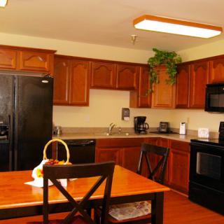 A cozy kitchen with wooden cabinets and black appliances, featuring a dining table.