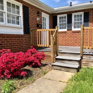 A welcoming house entrance with a small set of stairs, surrounded by vibrant red flowers and greenery.