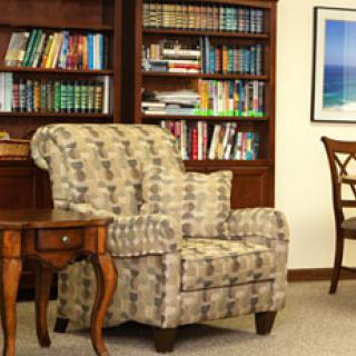 A cozy living room with an armchair, bookshelves filled with books, and a side table.