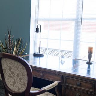 A serene workspace featuring a wooden desk and an upholstered chair with natural light streaming in.