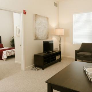 A modern living room with a television, lamp, armchair, and adjoining bedroom.