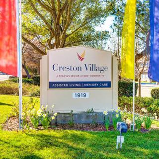 A sign for a retirement community named Creston Village, surrounded by colorful flags and well-maintained landscaping.