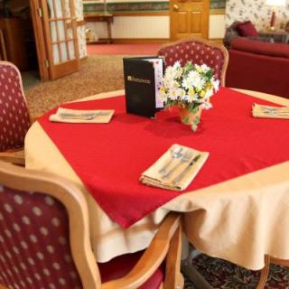A neatly set restaurant table with a red tablecloth, menu, and floral centerpiece.