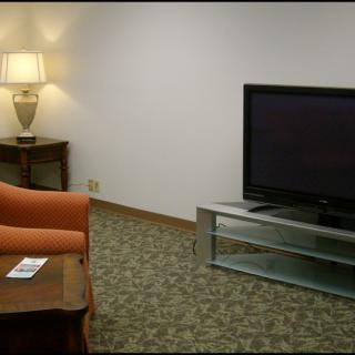 A cozy living room with a television, couch, lamp, and wooden table on a carpeted floor.