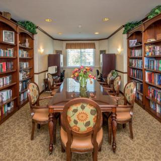 A cozy library room with a large wooden table, elegant chairs, and bookshelves filled with books on either side.