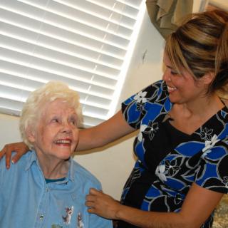 An elderly woman smiling at a caregiver who is providing support and companionship.