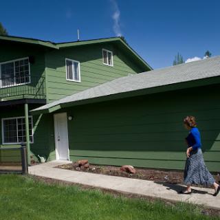 A woman walking by a green house on a sunny day.