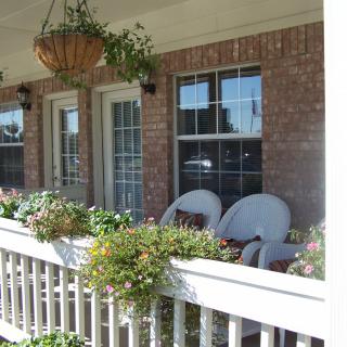A cozy porch with chairs, adorned with plants and flowers in pots and a hanging basket.