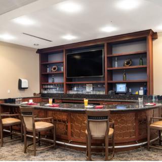 A cozy bar area with a polished counter, wooden shelves, and a mounted television.