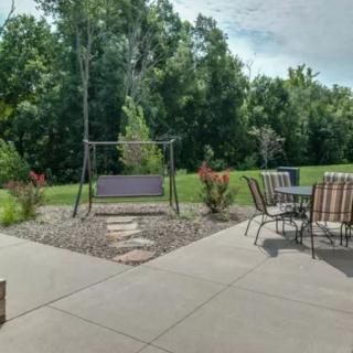 A serene backyard patio with outdoor seating and a swing, surrounded by lush greenery.
