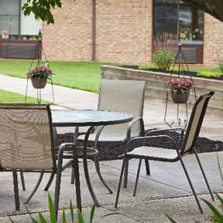 A cozy outdoor patio setup with a table and chairs, surrounded by greenery and hanging plants near a brick building.