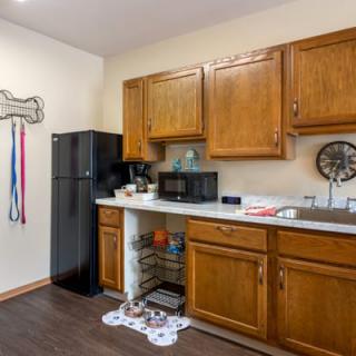 A small kitchen area with wooden cabinets, a refrigerator, microwave, and a sink.