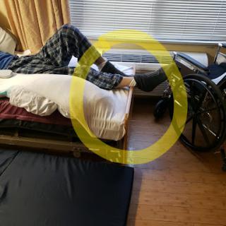 A person is resting with their legs elevated on a pillow, next to a wheelchair.