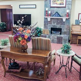 A cozy living room featuring elegant furniture, a stone fireplace, and a piano, decorated with vibrant flowers.