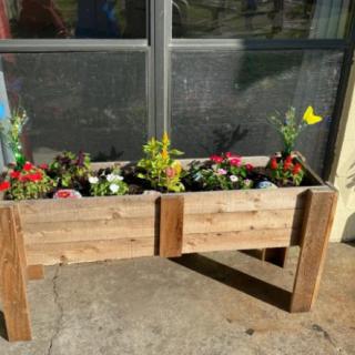 A wooden planter filled with colorful flowers, placed on an outdoor patio.