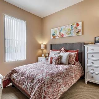 A cozy bedroom with patterned bedding, a bedside lamp, and decorative artwork on the wall.
