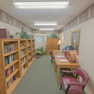 A quiet library room with bookshelves lining the walls, tables and chairs for reading.